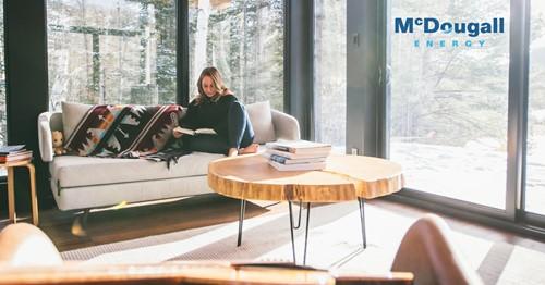 Shows a woman reading a book sitting on a large couch in a large room surrounded by windows