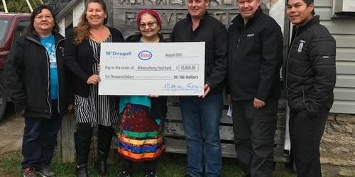 Shows 7 people outside holding a large cheque from McDougall Energy