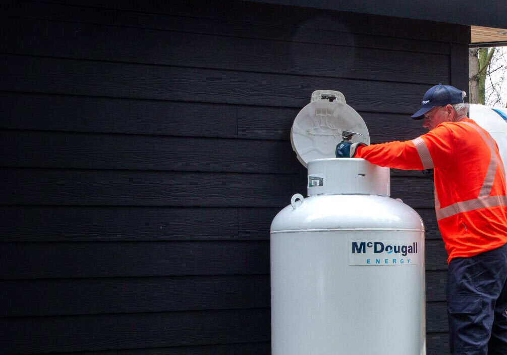 McDougall Energy Technician refilling residential propane tank outdoors during a scheduled automatic propane delivery.